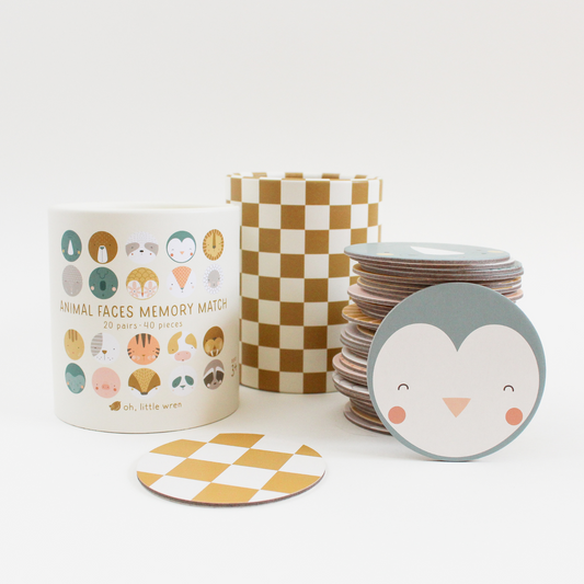 animal faces memory match game shown with white top on the left, then the base with yellow and white checkered and then the stack of circular pieces on the right. propped up and facing forward is a round penguin face piece. also shown in the back of the pieces, that is yellow and white checkered.