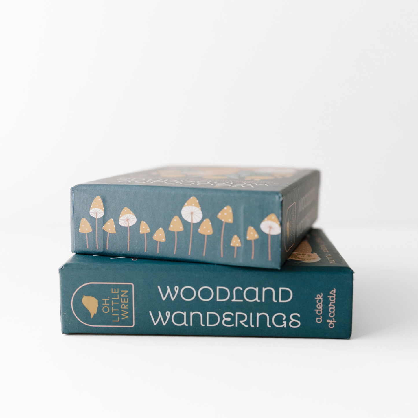 two boxes of woodland wanderings playing cards sit stacked, the bottom shows the side edge of the box and the top shows the top edge, decorated with mushrooms.