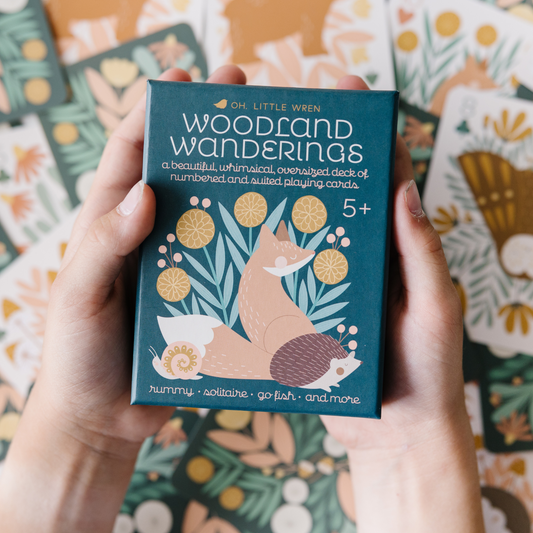 hands holding a box of woodland wandering playing cards. in the background are cards  arranged haphazardly.