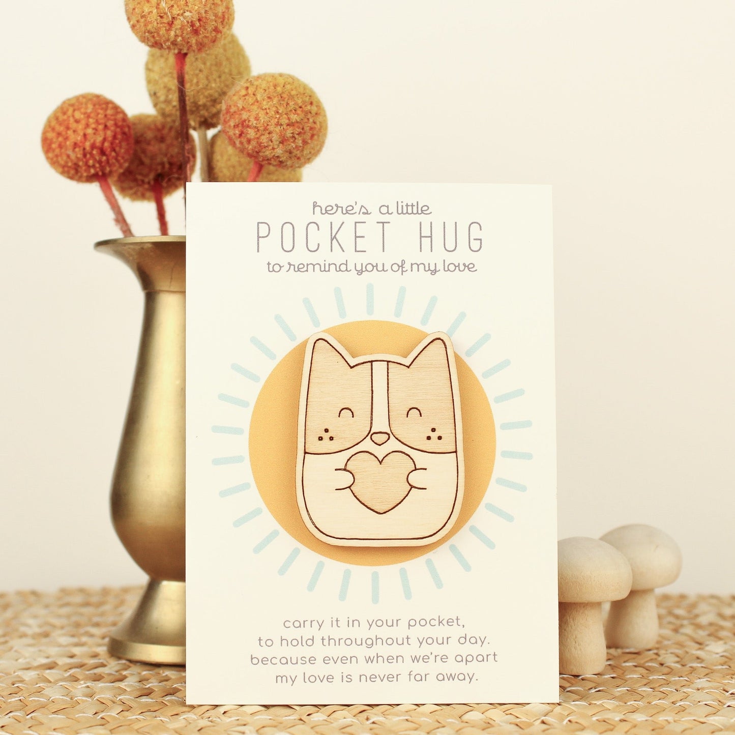 wooden dog pocket hugs is shown on its backer card propped up against a brass flower vase. card reads 'here's a little pocket hug to remind you of my love' and at the bottom 'carry it in your pocket, to hold throughout the day, because even when we're apart my love is never far away.'