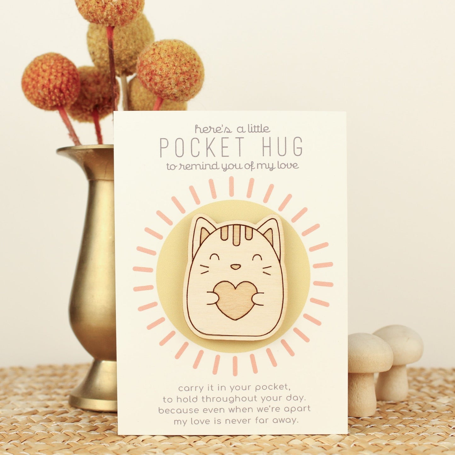 wooden cat pocket hugs is shown on its backer card propped up against a brass flower vase. card reads 'here's a little pocket hug to remind you of my love' and at the bottom 'carry it in your pocket, to hold throughout the day, because even when we're apart my love is never far away.'