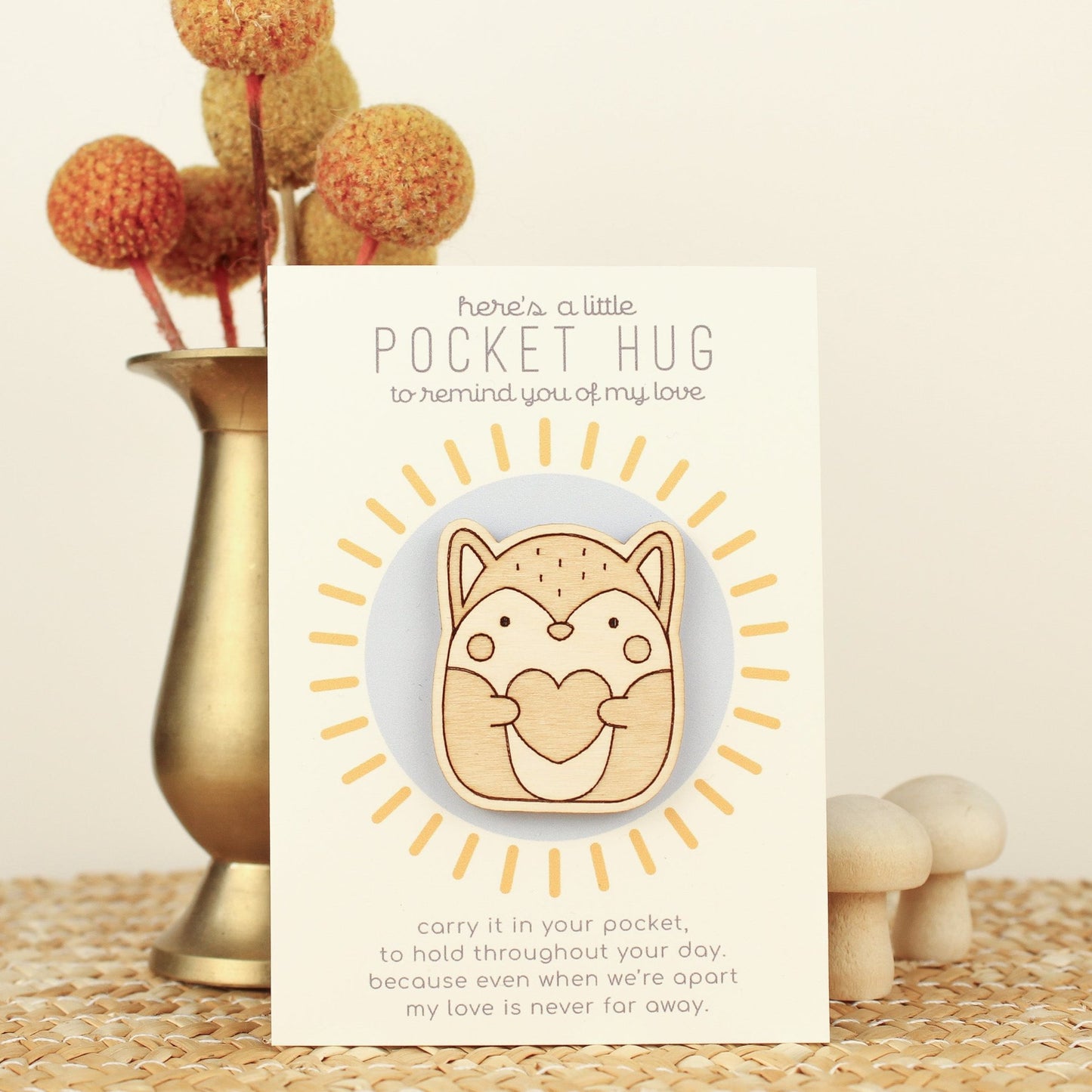 wooden fox pocket hug is shown on its backer card propped up against a brass flower vase. card reads 'here's a little pocket hug to remind you of my love' and at the bottom 'carry it in your pocket, to hold throughout the day, because even when we're apart my love is never far away.'