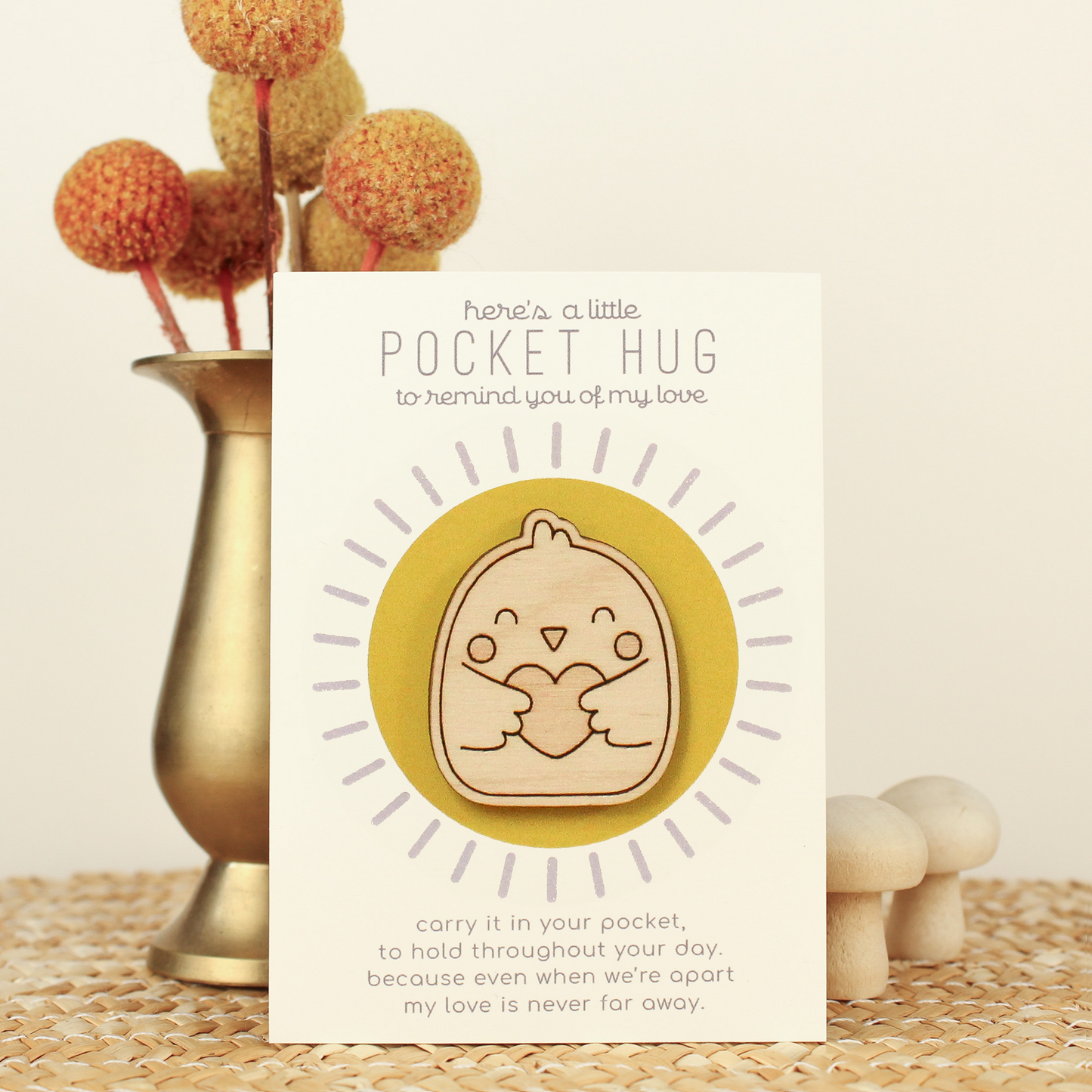 wooden bird pocket hugs is shown on its backer card propped up against a brass flower vase. card reads 'here's a little pocket hug to remind you of my love' and at the bottom 'carry it in your pocket, to hold throughout the day, because even when we're apart my love is never far away.'