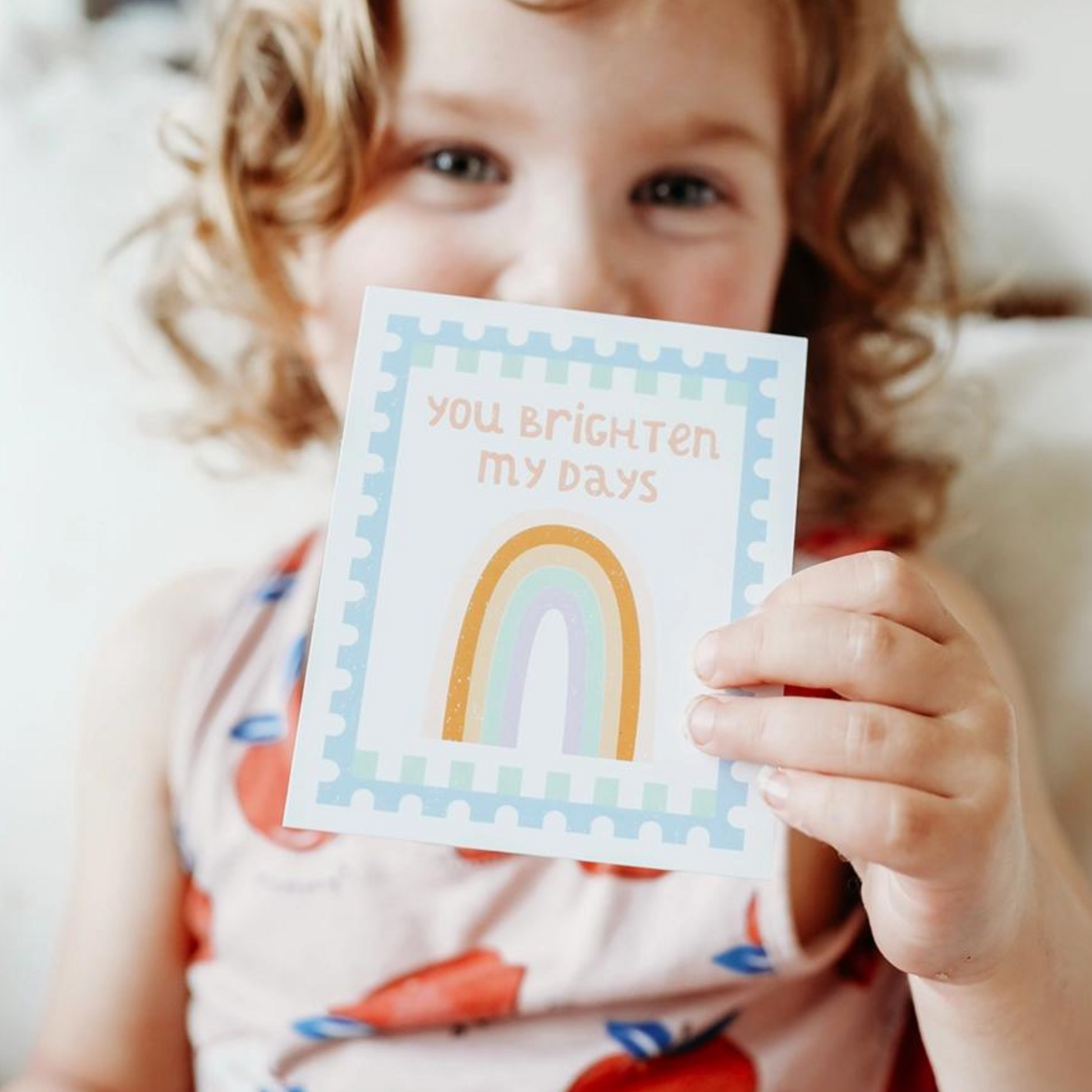 a child holds up a lunchbox note that reads 'you brighten my days' and has a picture of a rainbow.