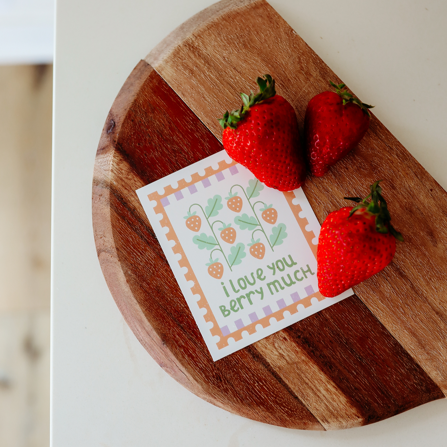 a lunchbox note with strawberries reads 'i love you berry much'. it's shown on a wood cutting board with strawberries.